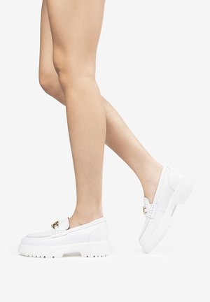 White leather slip-on loafers with a chunky white sole, featuring a gold-toned hardware accent and a stitched pattern along the upper.
