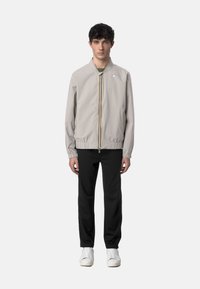 Giacca bomber grigia chiara con polsini ed elastico in vita, caratterizzata da una zip frontale e un design minimalista. Abbinata a pantaloni neri e sneakers bianche.