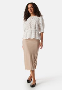 Witte getextureerde peplumtop met korte pofmouwen, gecombineerd met een lichtbeige midi-jurkenrok en zwarte ballerina's. Eenvoudig en elegant ontwerp.