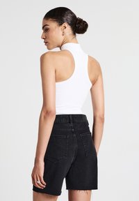Top blanc sans manches avec un col haut associé à un short en denim noir taille haute. Le short présente un ourlet brut et des poches arrière.