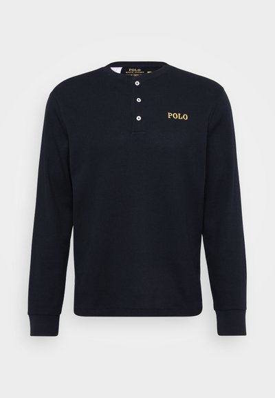 Camisa de manga longa azul-escura com um tecido texturizado em ribas, gola henley de dois botões e um logo "Polo" bordado a dourado no lado esquerdo do peito.