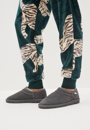 Pantofole grigie con morbida texture in camoscio e dettagli cuciti, abbinate a pantaloni verdi in pile con motivo a tigre beige e bianco.