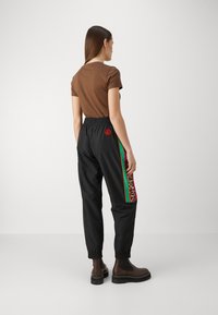 Schwarze Jogginghosen mit elastischem Bund, die einen mehrfarbigen Leopardenmuster-Seitenstreifen und ein braunes enges T-Shirt haben. Braune Stiefeletten.