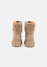 Bottines beige avec un bord en fourrure beige, extérieur lisse, semelle épaisse en caoutchouc et empeigne texturée pour la chaleur et le confort.