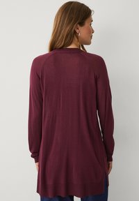 Bordeaux lange mouwen trui met een ontspannen pasvorm, zijsplitten en ribbeldetails bij de halslijn en zoom. Gladde brei textuur.