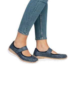 Chaussures Mary Jane en cuir navy avec un design perforé, semelle intermédiaire beige rembourrée et semelle extérieure en caoutchouc blanche, associées à un jean skinny bleu.