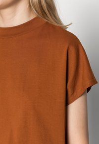 T-shirt color ruggine con scollatura rotonda e maniche corte arrotolate. Realizzato in un tessuto morbido e liscio con una finitura pulita.