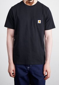 Černé bavlněné tričko s kulatým výstřihem a krátkým rukávem, které má malou kapsičku na hrudi a obdélníkovou nášivku s logem.