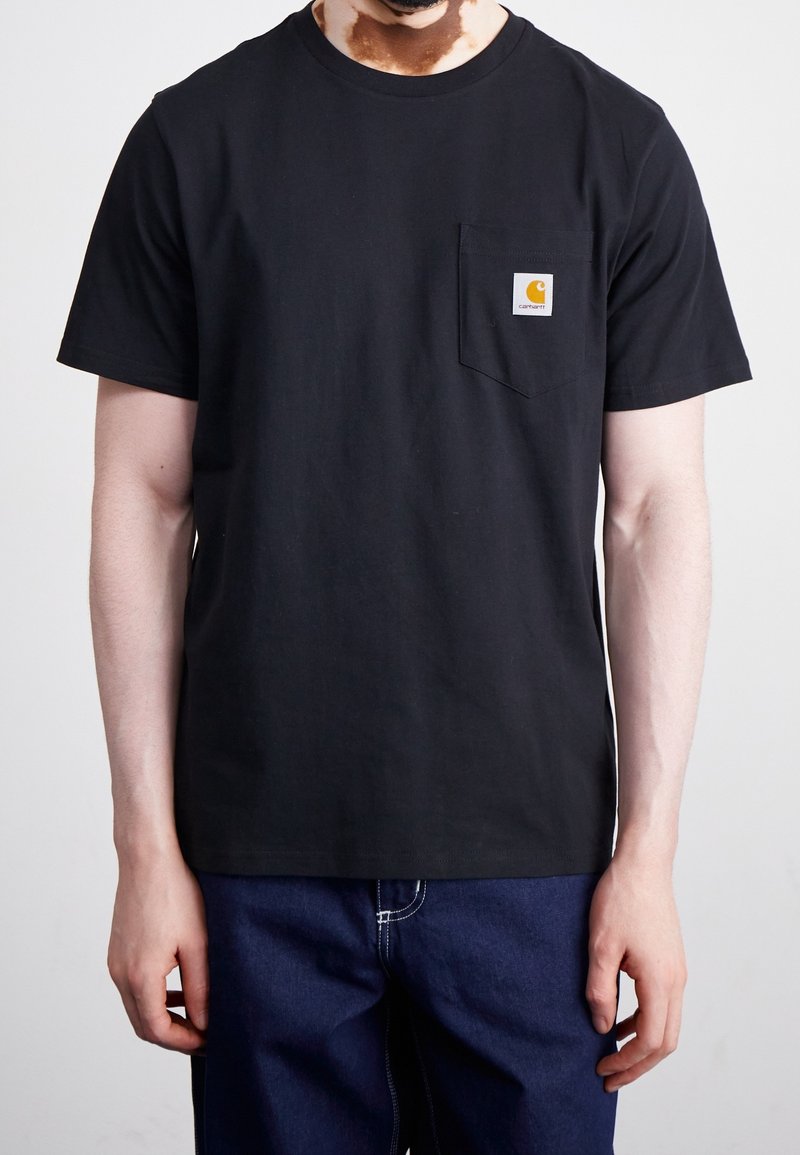 Černé bavlněné tričko s kulatým výstřihem a krátkým rukávem, které má malou kapsičku na hrudi a obdélníkovou nášivku s logem.