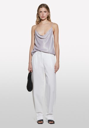 Camisole in satin viola chiaro con scollo a cowl, abbinato a pantaloni bianchi plissettati e sandali neri a piedi scoperti. Tiene una borsa nera texture.