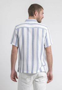 Chemise à manches courtes rayée en blanc et bleu avec un col boutonné, tissu texturé et ourlet droit. La vue de dos montre l'ajustement de la chemise.