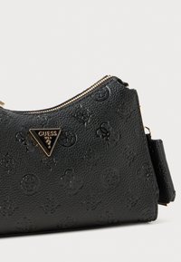 Svart texturerad Guess-handväska med präglade logotyper, guldtriangulärt varumärke och guldfärgad dragkedjestängning mot en vit bakgrund.