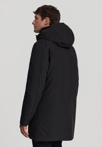 Parka nera con cappuccio, caratterizzata da una consistenza liscia, design di lunghezza intermedia e stile minimalista, adatta per il freddo.