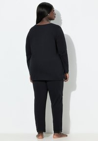 Zwart longsleeve shirt en bijpassende broek. Zachte stof, ontspannen pasvorm, met kanten rand aan de broekspijpen. Geen zichtbare patronen of logo's.