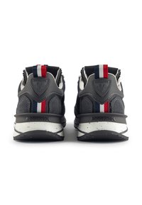 Zapatillas de ante gris con una suela exterior negra, que cuentan con una suela intermedia blanca con manchas, acentos a rayas rojas y azules en el talón, y detalles del logo.