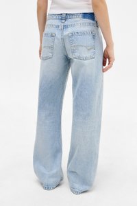 Jeans de pierna ancha de color azul claro con un acabado descolorido, que cuentan con dos bolsillos traseros y costuras amarillas.