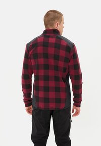 Rood en zwart geruite fleecejas met hoge kraag; heeft effen zwarte schouders en textielstof; de achterkant toont een getailleerd ontwerp.