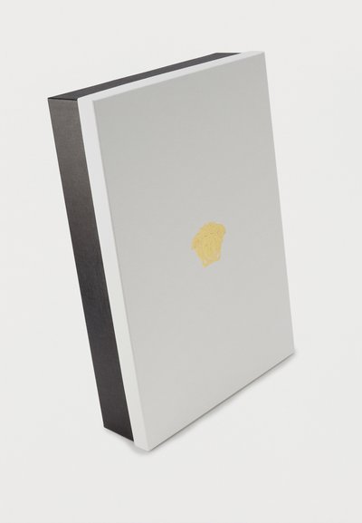 Λευκό ορθογώνιο κουτί με ένα μικρό χρυσό έμβλημα κεφαλής Μέδουσας στο κέντρο μπροστά, όρθιο σε λευκό φόντο.