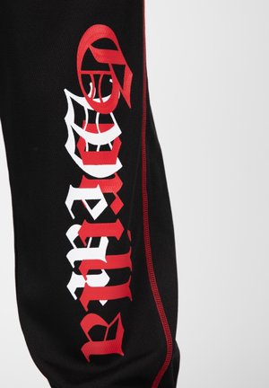 Zwarte joggers van stof met rode accenten hebben gedurfde witte en rode grafische teksten. Het ontwerp bevat complexe lettertypes en een sportieve uitstraling.