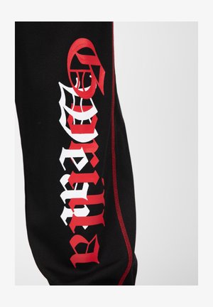 Zwarte joggers van stof met rode accenten hebben gedurfde witte en rode grafische teksten. Het ontwerp bevat complexe lettertypes en een sportieve uitstraling.