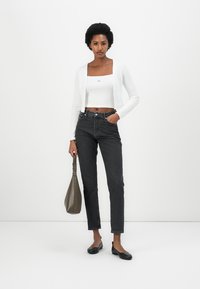 Hvit korterm cardigan, tettsittende hvit topp, svarte høytlivsjeans og svarte lavsko. Holder en brun skulderveske. Enkel design og dempede farger.