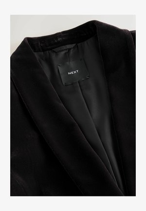 Črn žametni blazer z gladkim satenastim podlogom. Opazne značilnosti vključujejo ovratnik in oznako znotraj, ki prikazuje blagovno znamko "NEXT."