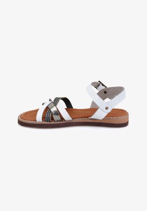 White strappy sandal with silver accents, brown insole, and textured black strap detail. Adjustable ankle strap with buckle closure.