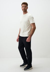 Weißes T-Shirt mit kurzen Ärmeln, kombiniert mit schwarzen Hosen und schwarzen Sneakers, das ein einfaches Design und eine neutrale Farbpalette aufweist.