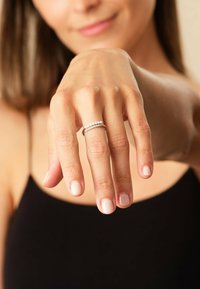 Anello d'argento con una fascia liscia e una fila di piccole perle tonde, esposto su una mano con unghie naturali e leggermente lucide.
