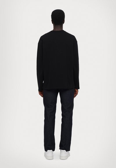 Black long-sleeve shirt with a relaxed fit, paired with dark denim jeans and white sneakers, viewed from the back against a plain background.
