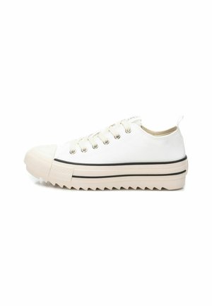 Zapatilla de lona blanca con puntera redondeada, ojetes metálicos, suela beige y patrón en zigzag en la suela exterior. Franja negra cerca de la suela para contraste.