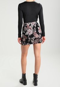 Un haut noir à manches longues associé à une mini jupe à motifs floraux présentant des fleurs roses et blanches sur fond noir, complété par des bottines noires.