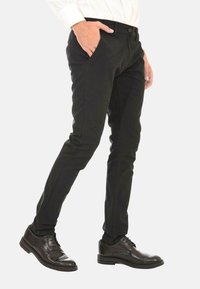 Pantaloni neri slim-fit con un motivo testurizzato, chiusura con bottone e tasche anteriori, abbinati a scarpe eleganti nere lucide.
