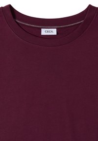 Gros plan d'un t-shirt violet foncé à col rond avec une étiquette blanche visible cousue à l'intérieur de l'encolure.