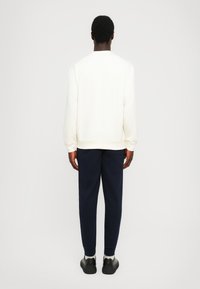 Sudadera blanca con cuello redondo y puños acanalados, combinada con pantalones de corte ajustado en azul marino oscuro y zapatillas negras. Tejido suave, ajuste relajado.