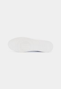 Semelle d'une sneaker blanche avec un motif de grip texturé et un logo de marque embossé au centre de la zone du talon.