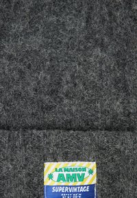 Gray textured fabric with fine fuzz, featuring a multicolored label reading "LA MAISON AMV SUPER VINTAGE" at the bottom.