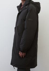 Zwarte gewatteerde parka-jas met een capuchon, drukknoopsluiting en een zijzak, met een soepele textuur en een knielange stijl.