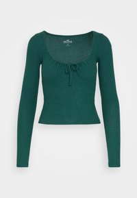 Pull long à manches longues en rib pourpre avec un décolleté carré. Présente un léger froncé et un détail de nœud au centre devant. Design extensible et ajusté.