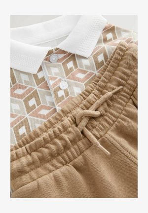 Short-sleeve polo in white, beige, and pink geometric print paired with tan jogger pants featuring an elastic waistband and drawstring.