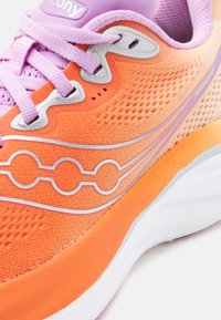 Κοντινό πλάνο πορτοκαλί και μοβ παπουτσιού τρεξίματος Saucony με επάνω μέρος από δίχτυ, ανακλαστικό λογότυπο και μοβ κορδόνια.