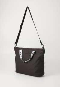 Svart tote-väska med justerbar axelrem och dubbla handtag, med fet vit "PUMA"-logotyp på framsidan.