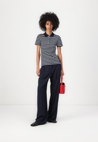 Striped polo skjorte i marineblått og hvitt, med krage og knapper. Kombinert med vide marineblå bukser og en liten rød veske.