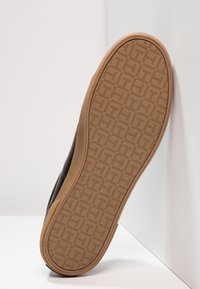 Černá podešev tenisky s texturovanou gumovou spodní částí, která se vyznačuje vzorem rybí kostry pro lepší trakci. Boční profil ukazuje hladký horní okraj.