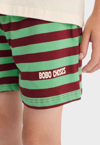 Enfant portant un short rayé vert et bordeaux avec l'inscription "BOBO CHOSES" sur le côté, à côté d'un t-shirt blanc.