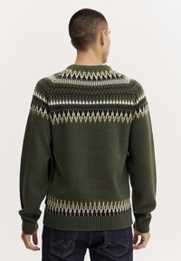 Dunkelgrüner Strickpullover mit geometrischen Mustern in Weiß, Schwarz und Gelb. Verfügt über einen Rundhalsausschnitt und gerippte Bündchen an den Ärmeln.