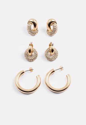 Drie paren gouden oorbellen: twee paren hebben ronde ontwerpen met kristallen, één paar heeft een gladde, ronde vorm.