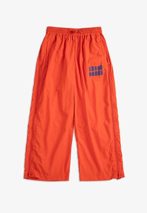 Jasnopomarańczowe spodnie o szerokich nogawkach z elastycznym paskiem w talii, bocznymi kieszeniami, pionowymi zamkami błyskawicznymi i niebieskim graficznym napisem na prawej udzie.