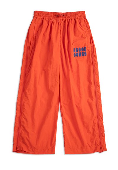Pantalon large orange vif avec taille élastique, poches latérales, fermetures éclair verticales et texte graphique bleu sur la cuisse droite.