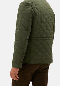 Veste matelassée en vert olive foncé, présentant un motif en losanges, une texture lisse et des poignets à bouton-pression. Conçue avec une coupe ajustée.